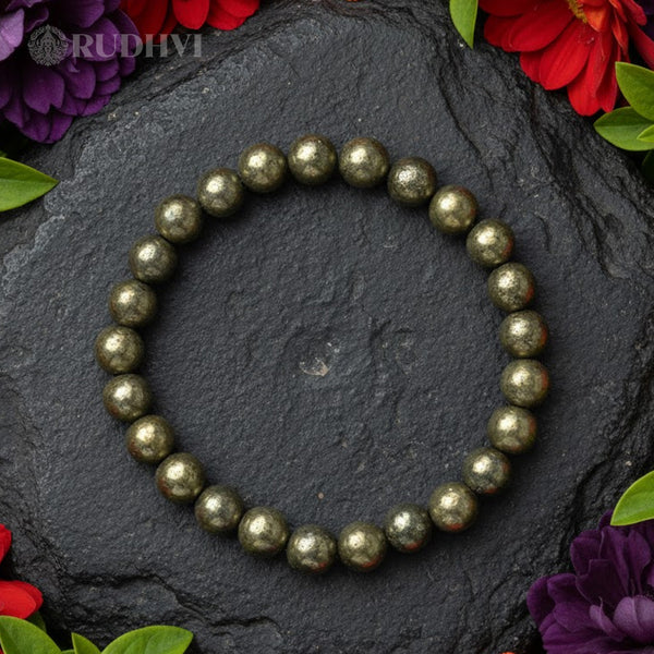 Pyrite beaded bracelet on a dark stone surface with flowers around