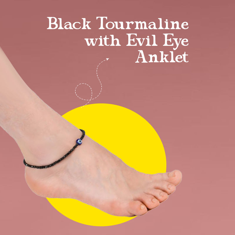 Anklet with black tourmaline and evil eye charm on a foot against a pink background